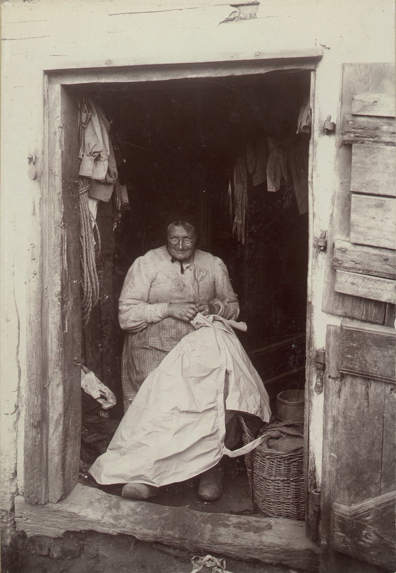 Kvinde der sidder i døråbning og syer på et hvidt klæde.