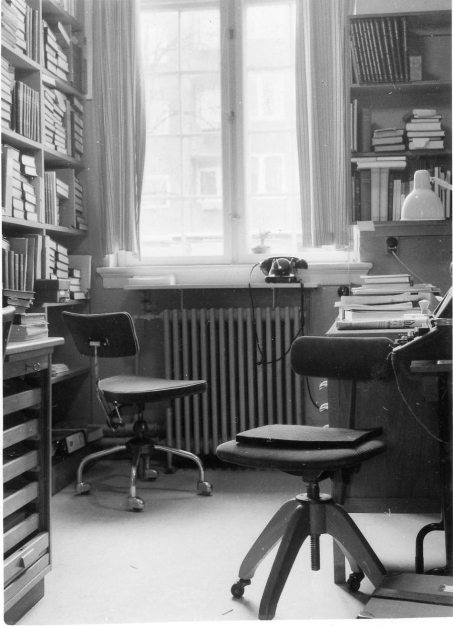 Ældre kontor med to stole, en drejeskivetelefon og fyldte reoler.